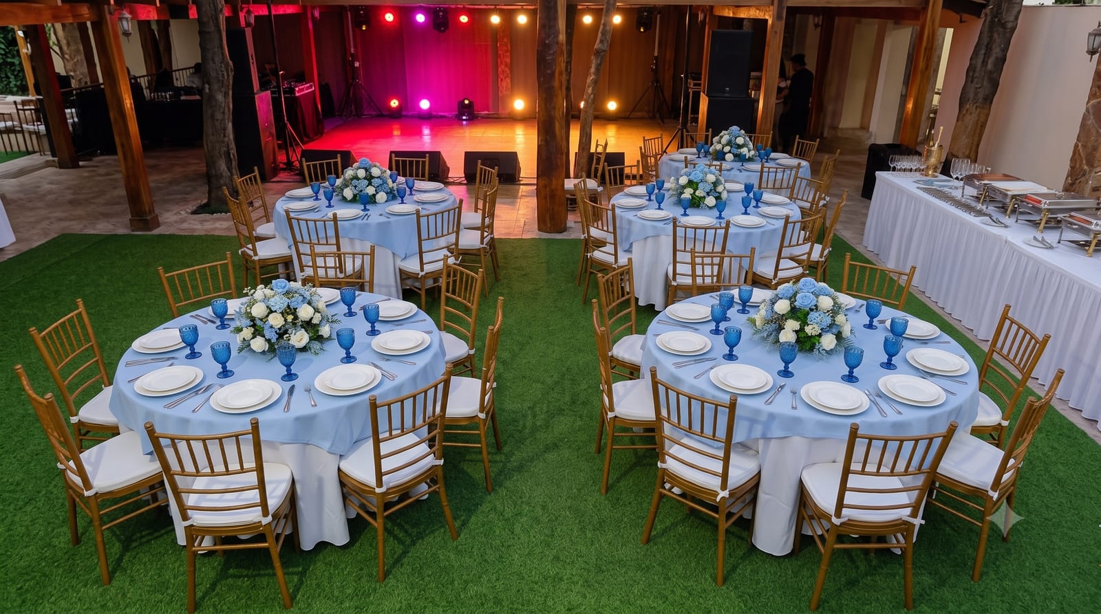 Montaje de evento al aire libre con mesas redondas, sillas chiavari doradas y copas azules