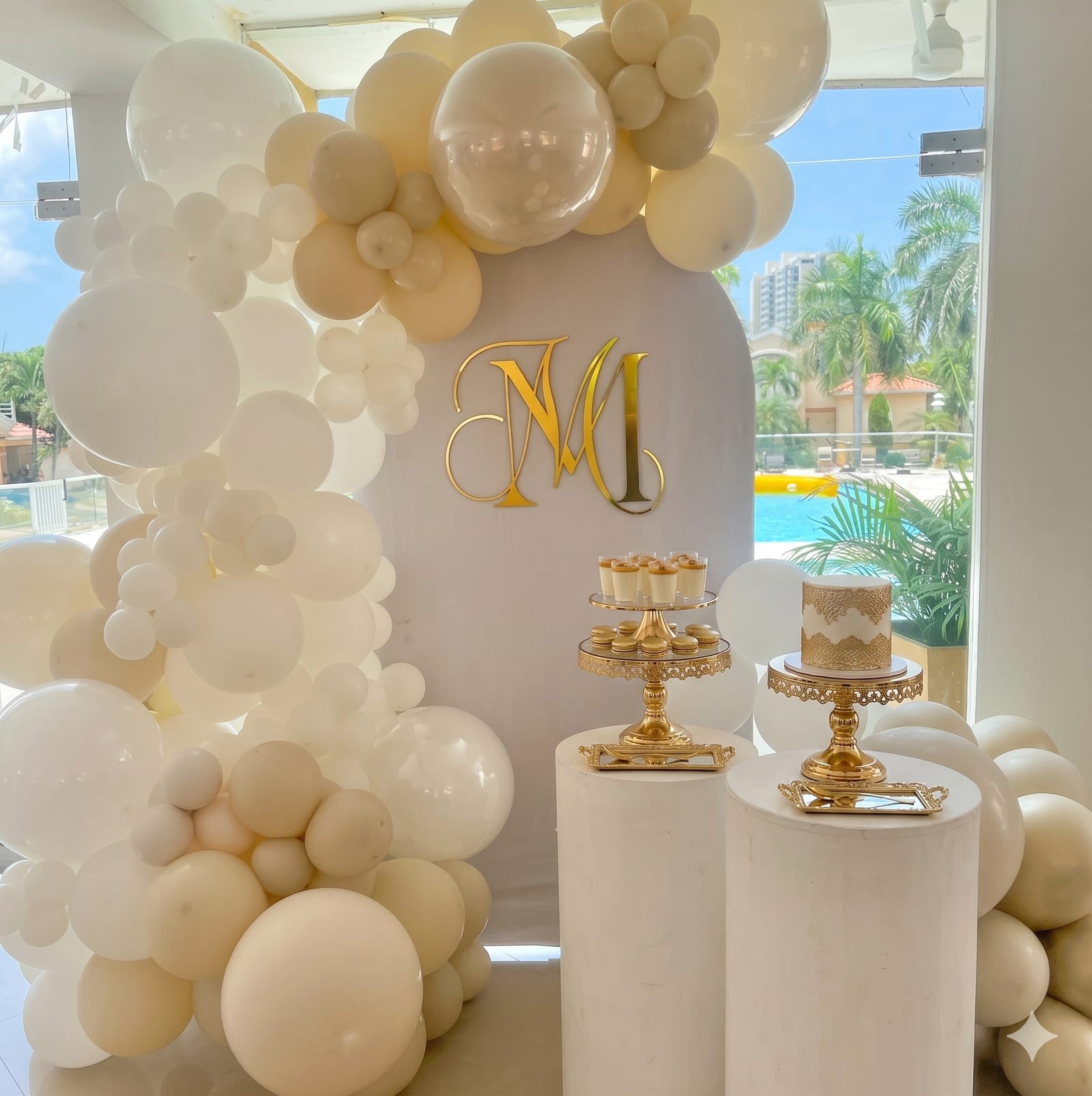 Mesa de postres decorada con globos, monograma dorado y bases de torta para eventos
